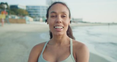 Neşeli bir kadın güzel sahil boyunca kablosuz kulaklık takarak neşeli bir şekilde koşar güneşli günün tadını çıkarır.