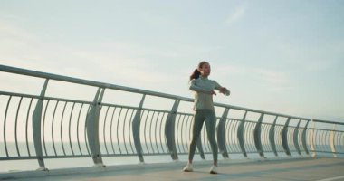 Genç bir kadın zarif bir şekilde sabah esnemesini muhteşem ve güzel bir rıhtım bölgesinde gerçekleştiriyor.