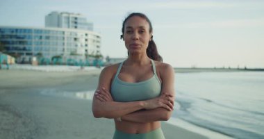 Kendine güvenen bir kadın sahilde şık bir spor kıyafetle poz verir, güç ve kararlılık saçar.