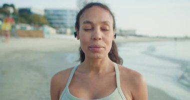 Genç bir kadın dingin plajda çalışmaktan zevk alıyor, kulaklıklarını takıyor ve sağlıklı bir yaşam tarzını benimsiyor.