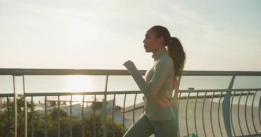 Güneş doğarken çarpıcı bir okyanus manzarası olan bir kadın tırabzan boyunca koşuyor. Sağlık, sağlık ve doğa..