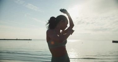 Sahilde zevkle egzersiz yapan, dingin bir zemine karşı canlılık gösteren bir kadının silüeti..