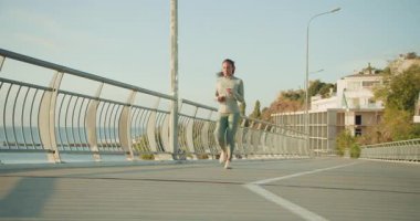 Formda bir kadın çarpıcı bir sahil yolunda zarif bir şekilde koşar, aktif ve sağlıklı bir yaşam tarzını benimser.