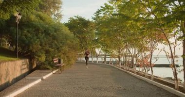 Çevresi yeşillik ve sakin sularla çevrili, manzaralı bir rıhtım yolunda koşan bir kadın, doğal güzelliğin tadını çıkarıyor.