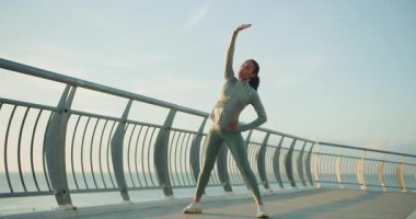 Bir kadın enerjik bir şekilde dinamik ve canlı dans figürleri sergiler. Su kenarında dinlendirici sabah egzersizleri sırasında.