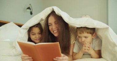 Kafkasyalı anne, kapalı kapak altında anlatım yaptı. Çocuklar, kapalı, anlamlı yüzleri dinliyorlar. Turuncu kitap sayfalarını nazikçe çeviriyorlar.