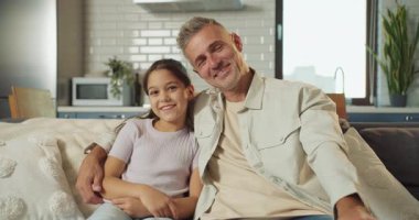 Baba ve kızı kanepeye yakın sıcak bir ışık, nazik bir sohbet ve rahat bir dairede sessiz bir bağ ile kucaklaşırlar, samimi bir şekilde.