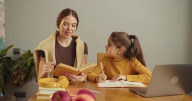 Anne, masada kızının yanında kitap okuyor. Ev içi ısıtma, dizüstü bilgisayar ve eğitim malzemeleri, veli ve çocuk değişimi.