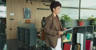 Siyah kadın tablet ve çantayla masaya yürüyor, eşyaları yerleştiriyor, çalışma alanını düzenliyor, kontrol programı, modern açık ofis,