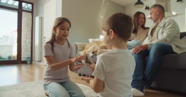 Ebeveynler izlerken beyaz kardeşler kanepenin önünde halıda oynuyorlar. Taş kağıt, makas, yumuşak halı ve sabah.