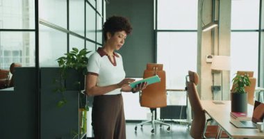 Yakındaki yeşil klasörü inceleyen kadın, günışığı ile modern çalışma ortamında yeşil dosyasını okuyan Afrikalı kadın.