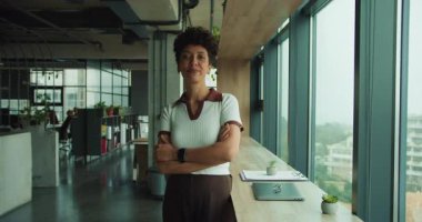 Siyahi kadın birlikte çalışma alanında güvenle gülümsüyor, girişimci kolları pencerenin yanında duruyor, parlak modern iç mekan.,