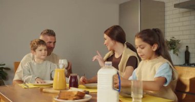 Aile, kahvaltı masasında toplanır. Sıcak tost, reçel, mısır gevreği, portakal suyu. Baba, çocukların annelerine katılır.