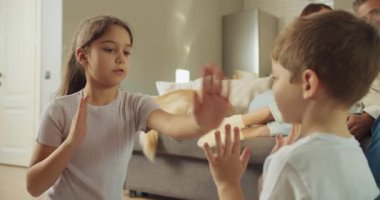 Çocuklar, ilgili ebeveynlerinin yanında el çırpmayı koordine ederler, kardeşler sıcak ev ortamında ritmik alkış tutarlar.