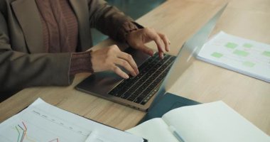 Ekip üyesi dizüstü bilgisayara hesap tablosu verilerini giriyor, çizelgeler ve raporlar masaya yayılıyor, düzenli daktilo ve sistemli odaklanma