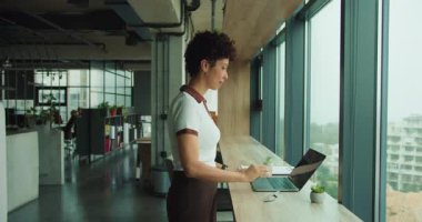 Siyah kadın dizüstü bilgisayarı pencere üstüne kuruyor sunucu webinar ekipmanları hazırlıyor ve ekranı, düzenli masayı, doğal gün ışığını kontrol ediyor.,