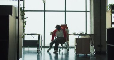 siyah kurucu ofis sandalyesini pencere döndürür, masa ve bitkilerle modern çatı katı çalışma alanı, görevler arasında şakacı bir mola, enerjik