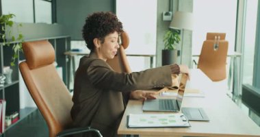 siyahi kadın sunum için dizüstü bilgisayarı açıyor, slaytları kontrol ediyor, notları ayarlıyor, yakınlarda deri çanta, doğal ışık,