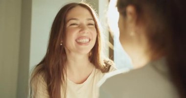 Beyaz anne, güneşli odada kızıyla birlikte gülüyor. Güçlü lensler, parlak arka plan ışıkları. Neşeli, neşeli, neşeli, neşeli bir pencere.