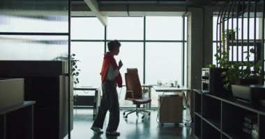 Siyah yönetici ofisin içinde yürüyor, büyük pencereleri ve masaları olan bir çatı katı, sakin volta ve gözlem