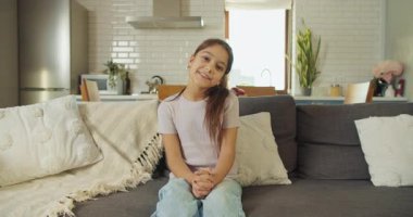 Kanepede oturan genç kız, rahat oturma odasında kameraya konuşuyor, samimi konuşmalar, anlamlı jestler ve parlak bir gülümsemeyle.,