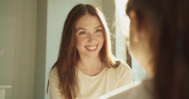 Güneşli odada gülümseyen kadın sıcak bir sohbet ve görünmeyen arkadaşla göz teması kuruyor.