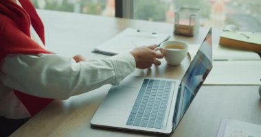 Masa başı dizüstü bilgisayar ve kahve fincanı, fincana uzanan eller ve daktilo, masadaki belgeler ve çizelgeler, görevler arasında odaklanmış mola,