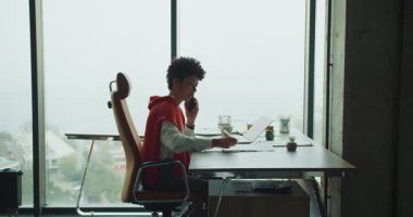 Pencere masasında kahvesini yudumlayan, dizüstü bilgisayarını ve not defterini inceleyen, şehrin ufuk çizgisi tavan penceresinden geçen siyah serbest yazar.,