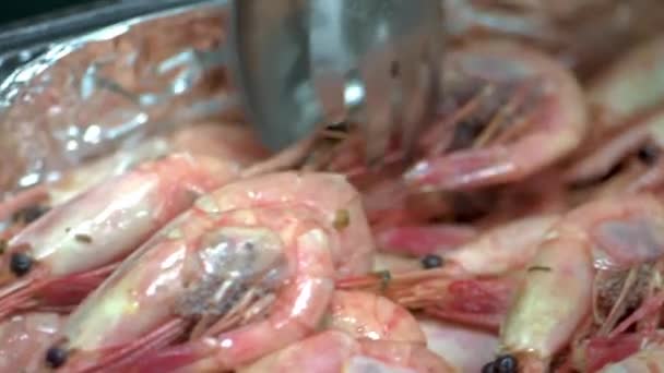 Lo chef con pinze da cucina mette gamberetti bollenti in scatola di plastica su lamina di metallo. HD — Video Stock