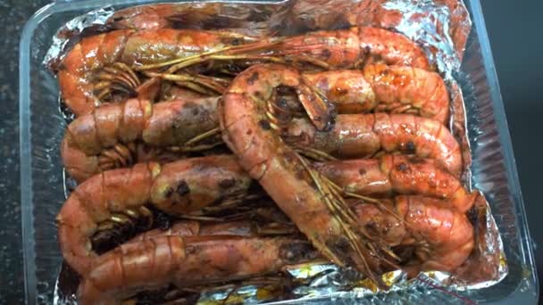 Chef con pinzas de cocina pone gambas fritas en caja de plástico sobre papel de aluminio. HD — Vídeo de stock