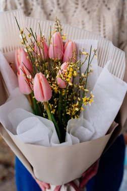 Bej pakette pembe lale buketi örülmüş örgü ören çiçekçi kızın ellerinde..