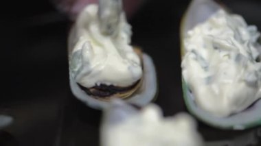 Kaşıklı şef kabuklu midyelerin üzerine peynir sosu serer. Yakın plan. HD