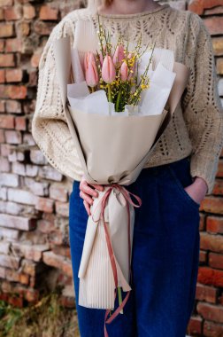 Bej pakette pembe lale buketi örülmüş örgü ören çiçekçi kızın ellerinde..