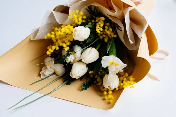 Beyaz arka planda bej pakette beyaz lale, narsis ve mimoza demeti..