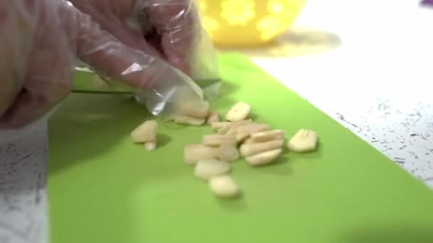 Koki restoran memotong bawang putih di atas papan potong plastik. Chef memakai sarung tangan. HD — Stok Video