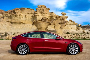 Bolnuevo, Murcia, İspanya - 7 Şubat 2020: Akdeniz kıyısında kaya oluşumlu kırmızı bir Tesla Model 3 elektrikli araba ve Bolnuevo, Murcia, İspanya 'da mavi gökyüzü.