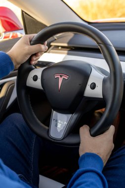 Murcia, İspanya - 1 Aralık 2019: genç adam bir Tesla arabası kullanıyor ve direksiyonu elinde tutuyor. Tesla 'nın amblemi, Tesla, Inc.' nin ürettiği ve sattığı, orta büyüklükte, elektrikli otomobil Model 3 'ün tekerleğinde..