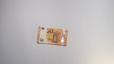 Bir adamın 50 avroluk banknotları gökkuşağı şeklinde yerleştirdiği statik bir görüntü. Arkaplan beyaz renktir.