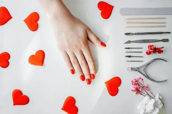 Manicured woman\'s nails with red nail polish. Tools of a manicure set, red hearts on white.