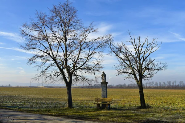 Austria, rest area with bench and statue of saint from 17th century in agricultural area