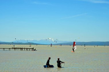 Podersdorf, Avusturya - 09 Mayıs 2021: Kimliği belirsiz insanlar, uçurtma ve rüzgar sörfçüleriyle Neusiedlersee, Burgenland 'deki sahil tatil beldesinde su sporu,