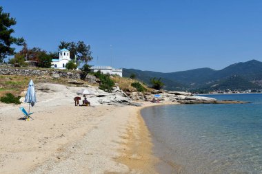 Iraklitsa, Yunanistan - 24 Haziran 2021: Kavala yakınlarındaki Iraklitsa kumsalında kimliği belirsiz insanlar ve tepedeki ortodoks şapeli