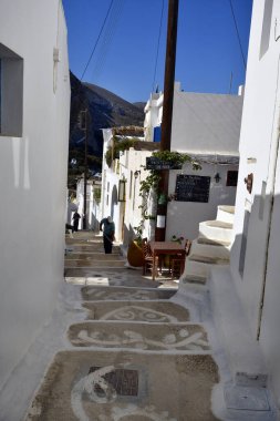 Amorgos, Yunanistan - 10 Eylül 2025: Bilinmeyen işçiler, Ege Denizi 'ndeki muhteşem bir Cycladic adası olan Amorgos adasındaki Lagkada dağ köyündeki tablolarla tipik dar kaldırımlardan birini yeniden işlediler