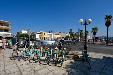 Kos, Greece - September 15, 2025: Dolphin fountain in roundabout Dolphin Square and rental bikes, unidentified people on harborside in the capital of Kos Island