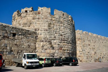 Kos, Greece - September 16, 2025:  Various vehicles are parked along the castle wall with battlements along the harbor of kos town