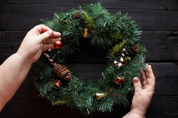 Christmas wreath on black wooden background. Grandma hands.