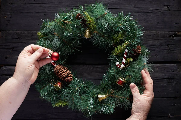 Christmas wreath on black wooden background. Grandma hands.