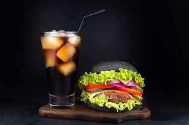 Koyu arkaplanda bir bardak kolayla büyük tek bir çizburger.