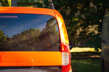 Turuncu arabanın arka penceresi yaz güneşli bir günde, dikiz manzaralı caddeye park edilmiş. Çıkartma veya çıkartma için modelleme