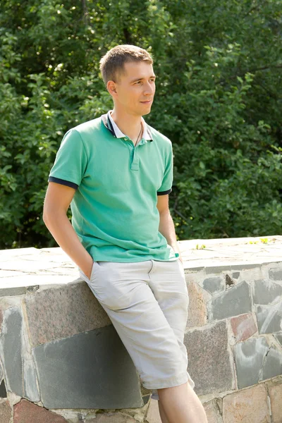 Attractive young man looking sideways and leaning against a stone parapet